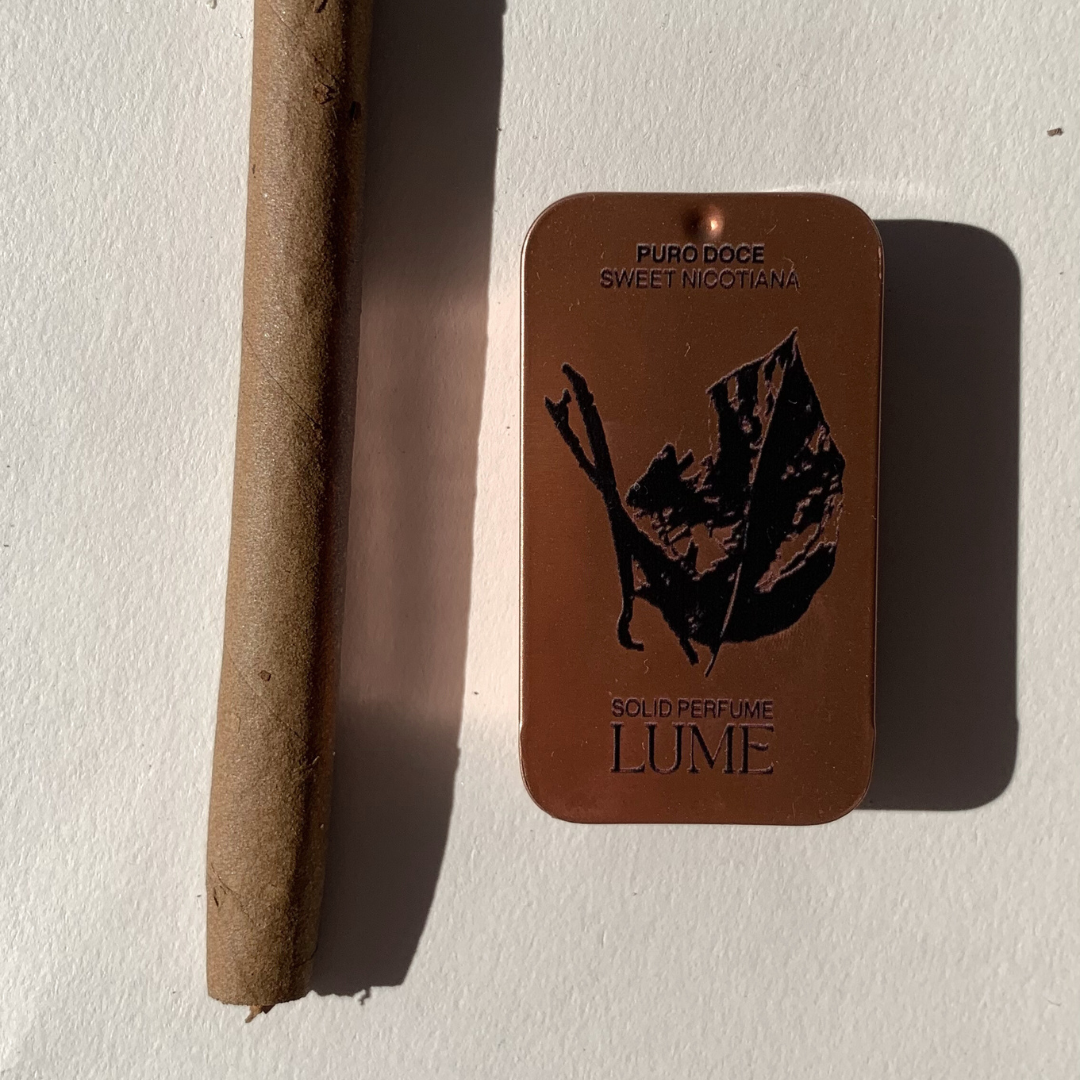 Top view of a solid perfume in a metal tin, next to a Swisher Sweet cigar.